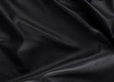 A close-up of draped black leather fabric with a smooth, pebbled texture and soft folds.