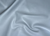 A close-up of draped light gray faux leather or vinyl fabric with a smooth, slightly glossy texture.