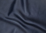 A close-up of dark navy blue textured leather fabric with soft folds and creases.