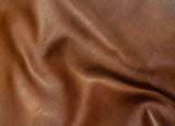 A close-up of draped brown leather fabric showing its pebbled texture and soft folds.