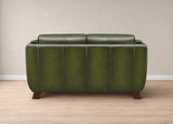 An olive green leather loveseat sofa shown from the back, featuring vertical channel tufting and dark brown wooden legs, set against a neutral beige wall and light wood floor.
