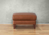 Brown leather ottoman on a wooden floor with a gray wall background