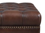 Close-up of a brown leather ottoman with tufted design and nailhead trim.