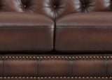 Close-up of a brown leather sofa with tufted backrest and nailhead trim.