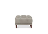A square tufted ottoman in light taupe fabric with dark brown wooden legs, shown against a plain white background.