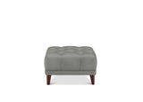 A square tufted ottoman in a muted gray fabric, supported by four dark brown wooden legs, shown against a plain white background.