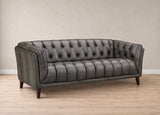 A dark gray tufted leather loveseat sofa with dark wooden legs, set against a neutral beige wall and light wood floor.