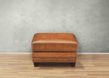 Brown leather ottoman on a wooden floor with a gray wall background