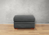 Gray ottoman with wooden legs on a wooden floor against a gray wall