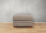 Gray ottoman with wooden legs on a wooden floor against a gray wall
