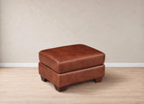 A brown leather ottoman with a stacked design and dark wooden legs, set against a neutral beige wall and light wood floor.