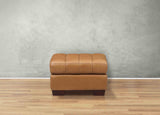 Tan leather ottoman on a wooden floor with a gray wall background