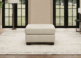 Beige ottoman on a white rug in a room with large windows.