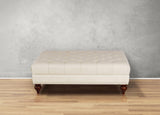 Beige tufted ottoman on a wooden floor with a gray wall background