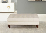 Beige tufted ottoman with wooden legs on a gray carpet