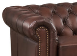 Brown leather sofa with tufted backrest and nailhead trim on a white background