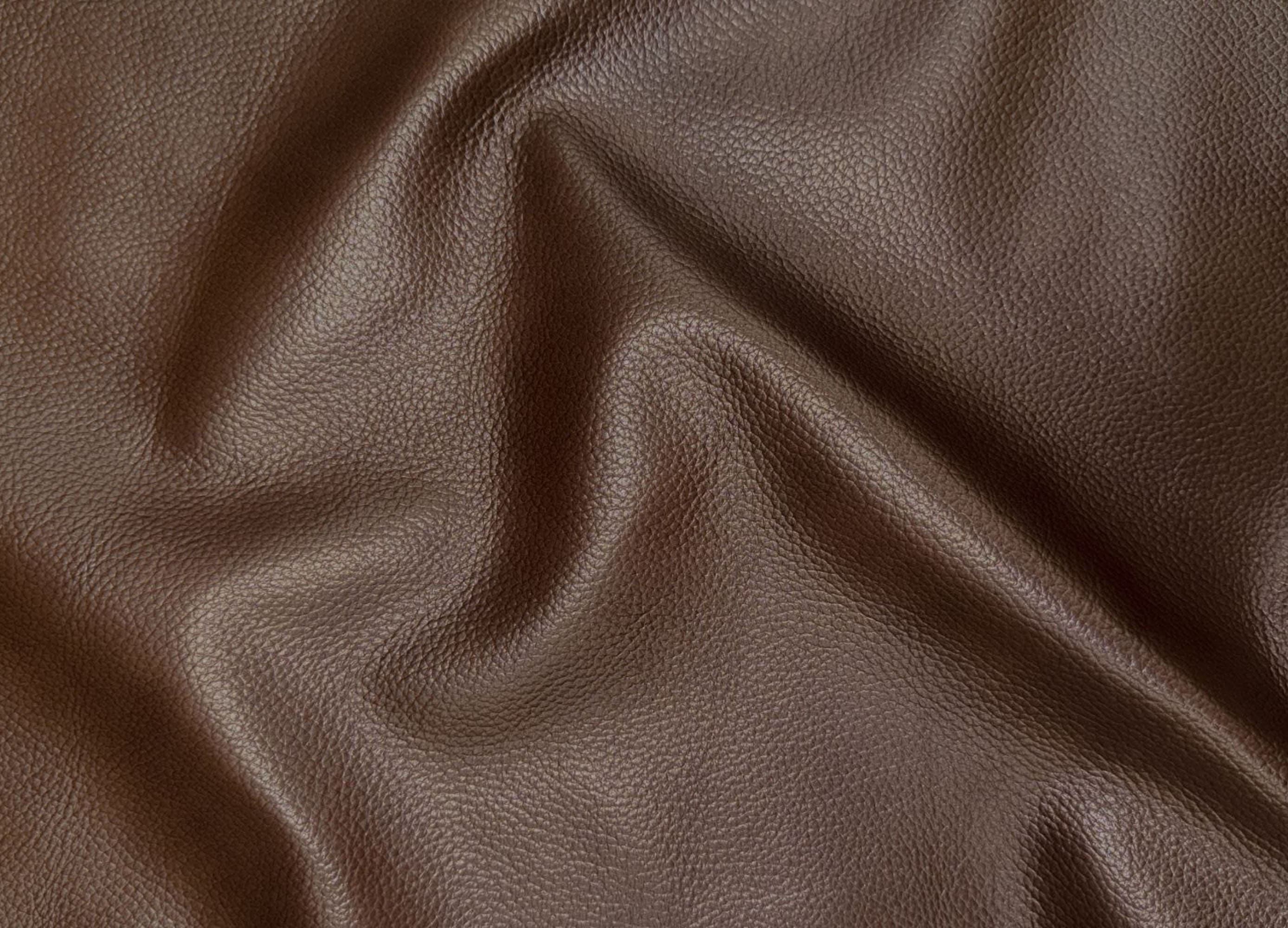 A close-up of draped brown leather fabric with a pebbled texture and soft folds.