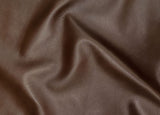 A close-up of draped brown leather fabric with a pebbled texture and soft folds.