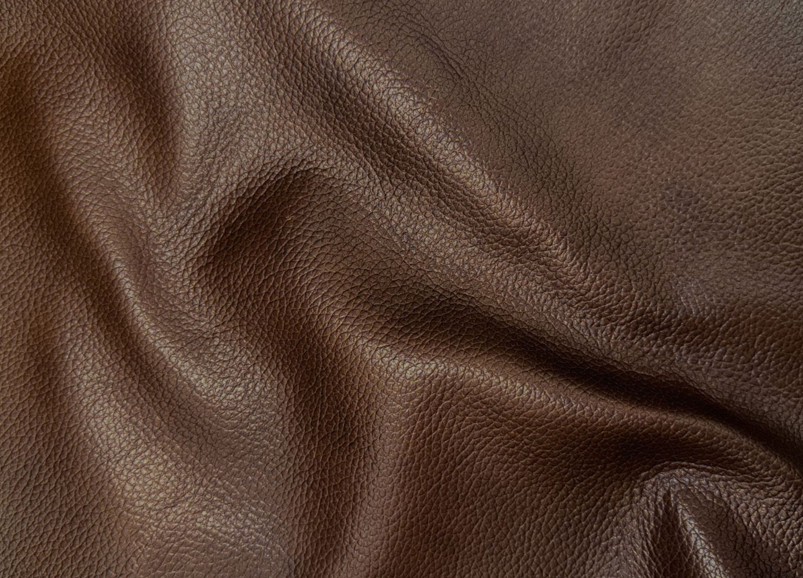 A close-up of dark brown textured leather with soft folds and a pebbled grain surface.