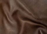 A close-up of dark brown textured leather with soft folds and a pebbled grain surface.