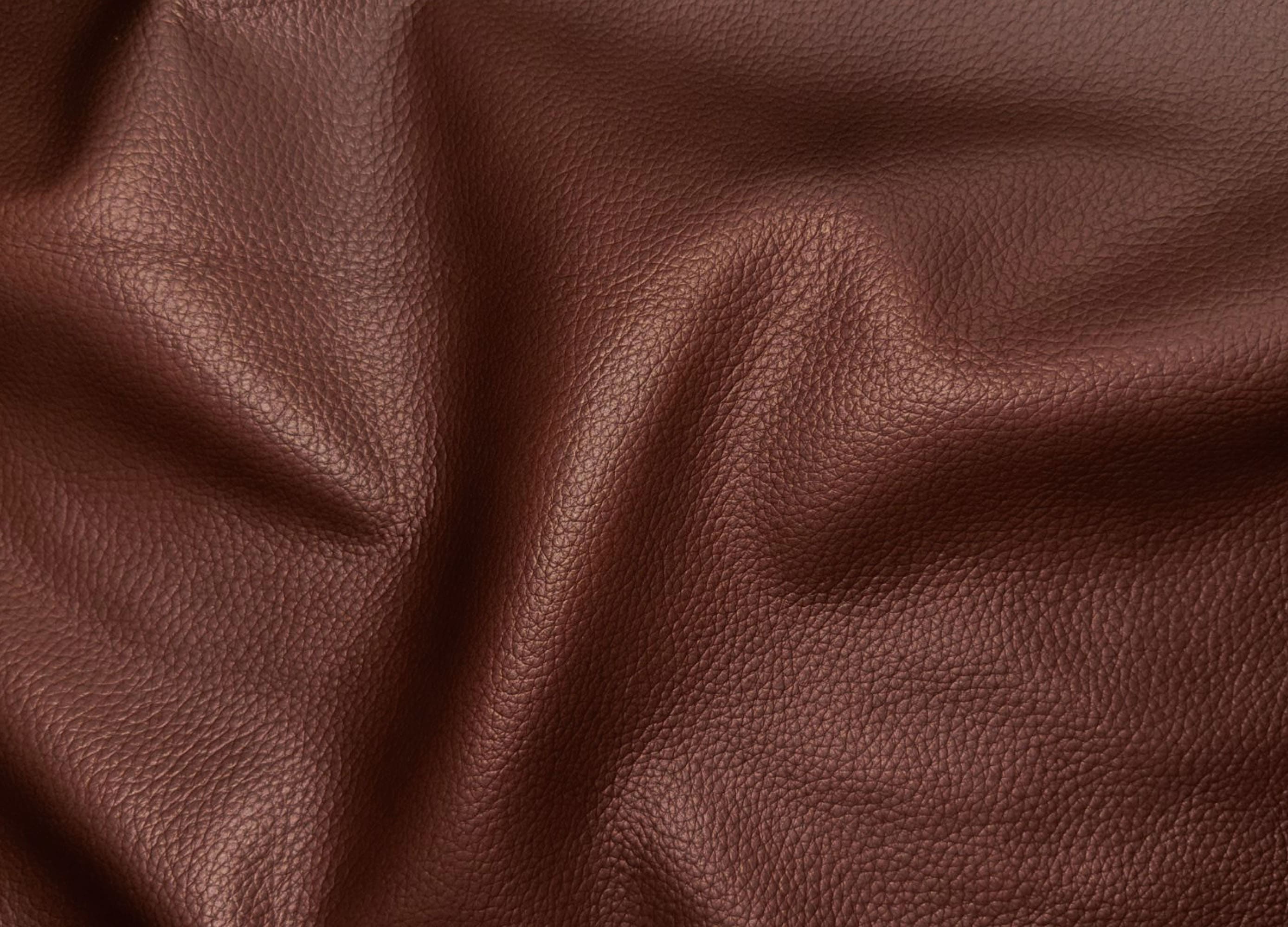 A close-up of draped brown pebbled leather fabric showing its texture and soft folds.