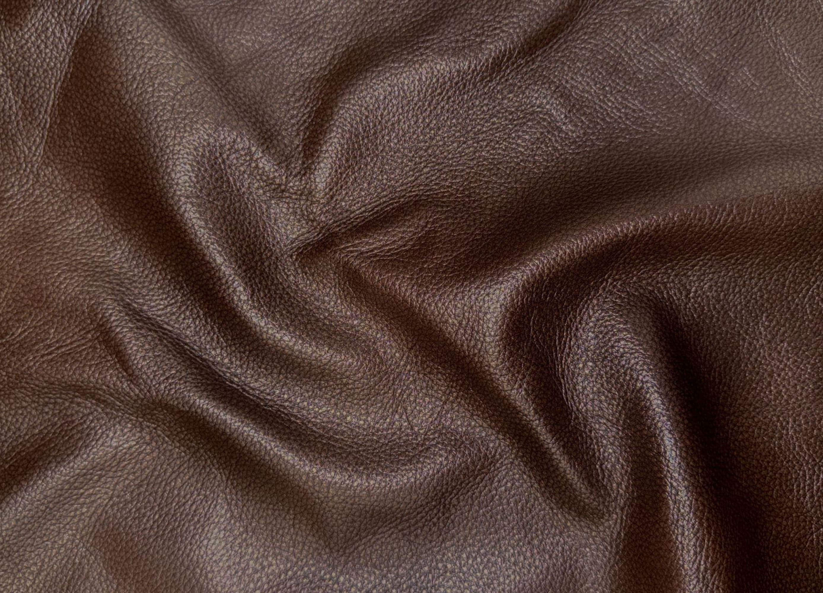 A close-up of draped dark brown textured leather fabric with visible grain and soft folds.