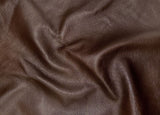 A close-up of draped dark brown textured leather fabric with visible grain and soft folds.