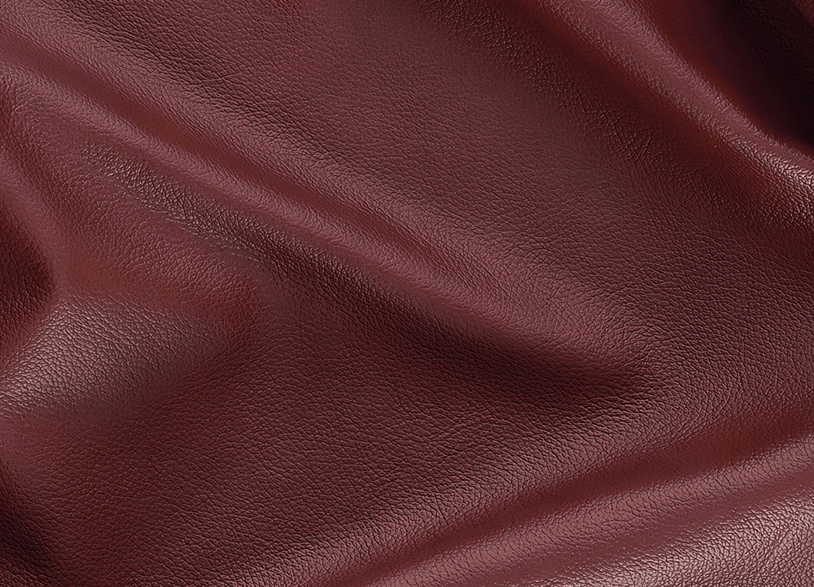 A close-up of draped burgundy leather fabric showing its fine grain texture and soft folds.