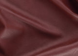 A close-up of draped burgundy leather fabric showing its fine grain texture and soft folds.