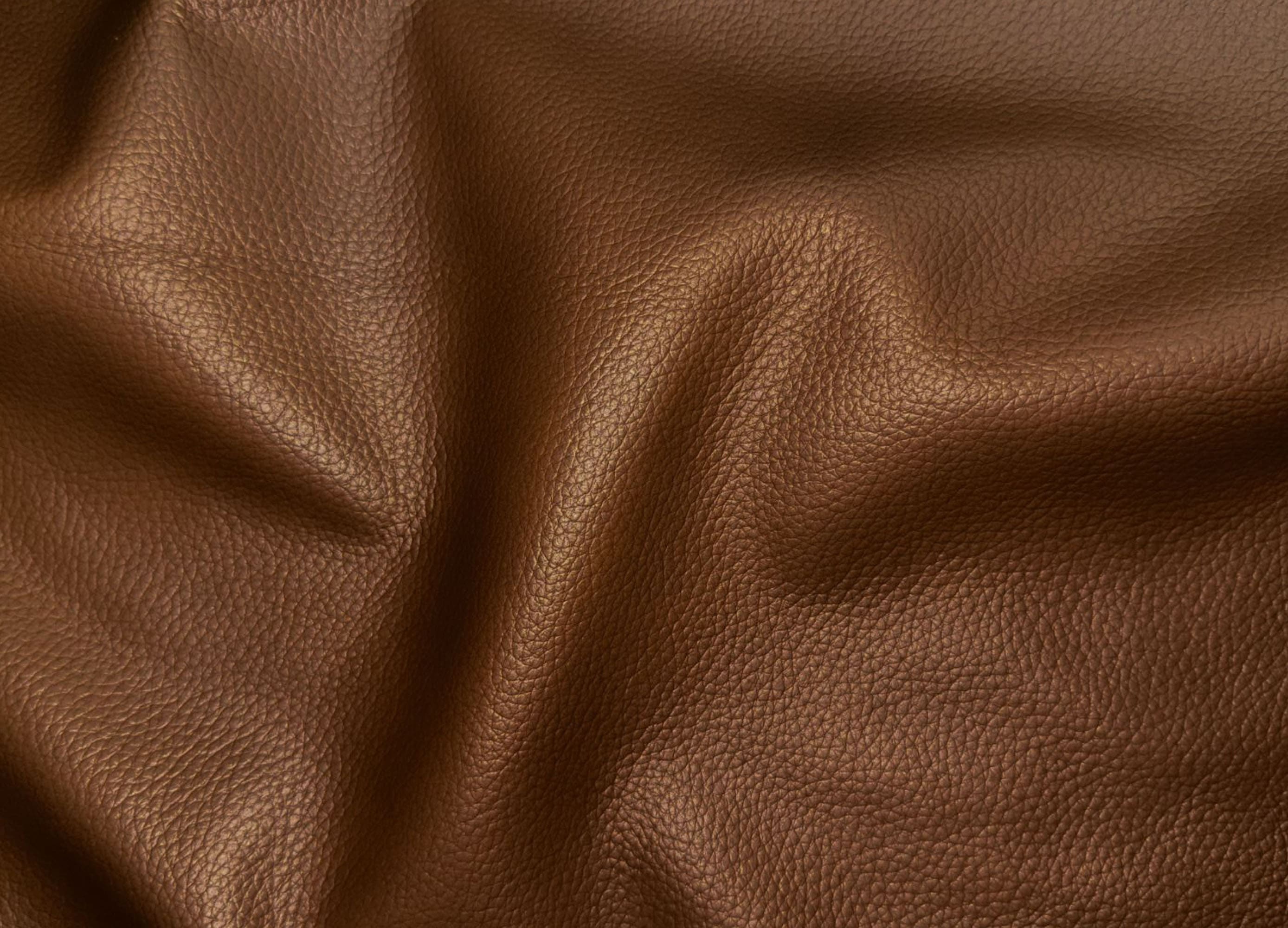 A close-up of draped brown pebbled leather fabric showing its texture and soft folds.