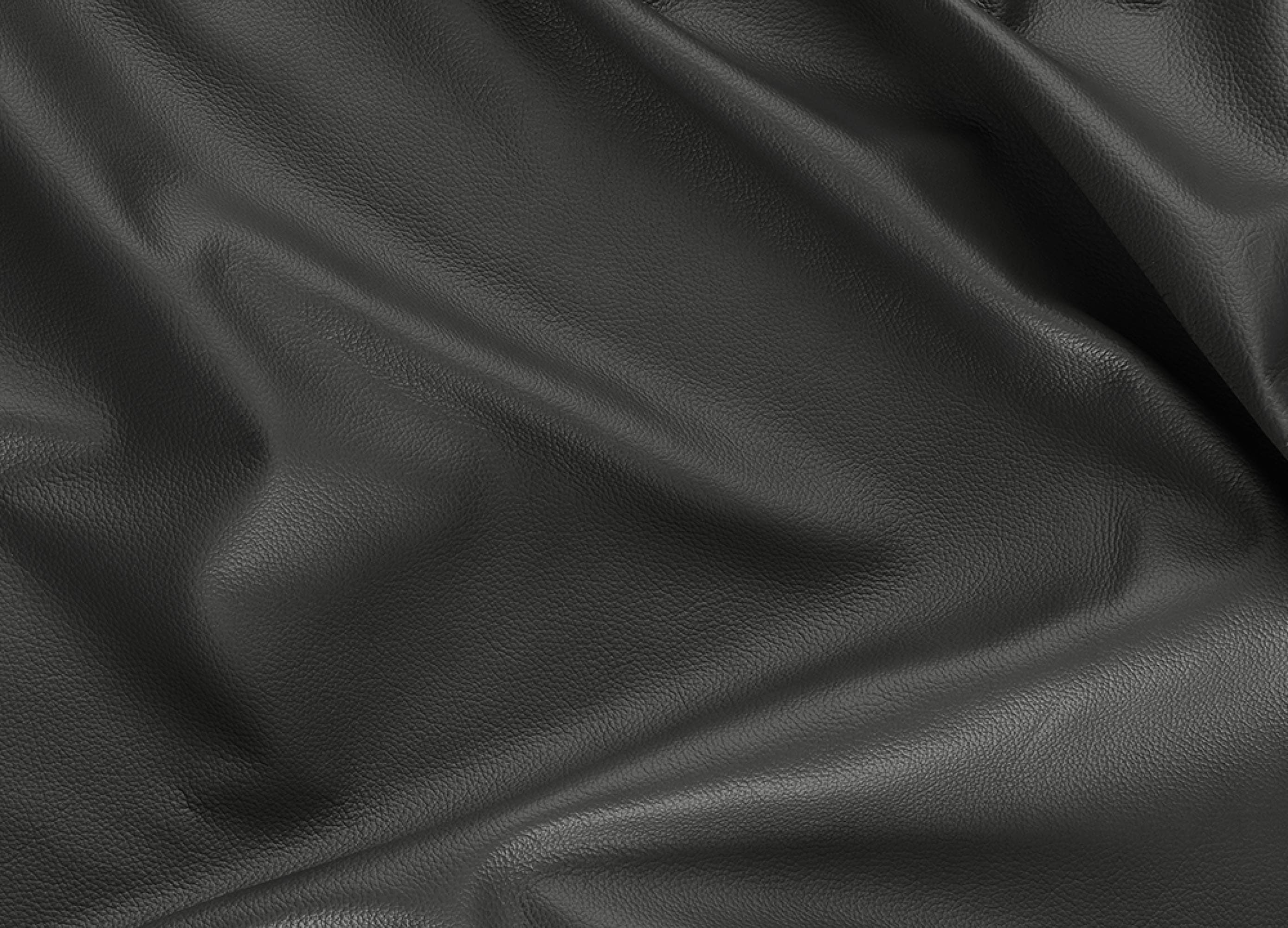 A close-up of draped black leather fabric with a smooth, pebbled texture and soft folds.