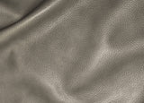 A close-up of textured leather material in a warm taupe-gray color, showing the pebbled grain and soft folds.