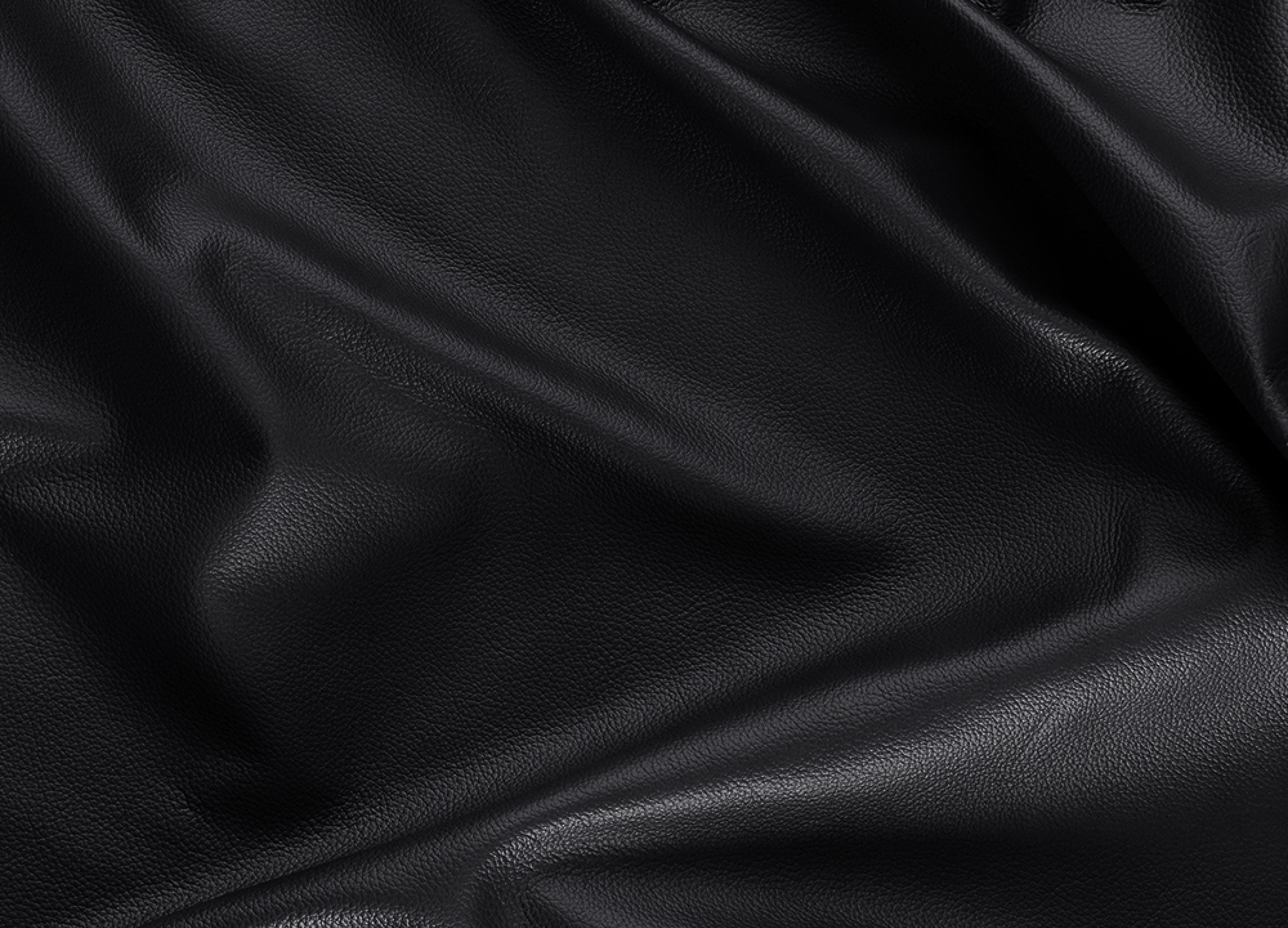 A close-up of draped black leather fabric with a smooth, pebbled texture and soft folds.