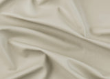 A close-up of draped light beige leather fabric with soft folds and a smooth texture.