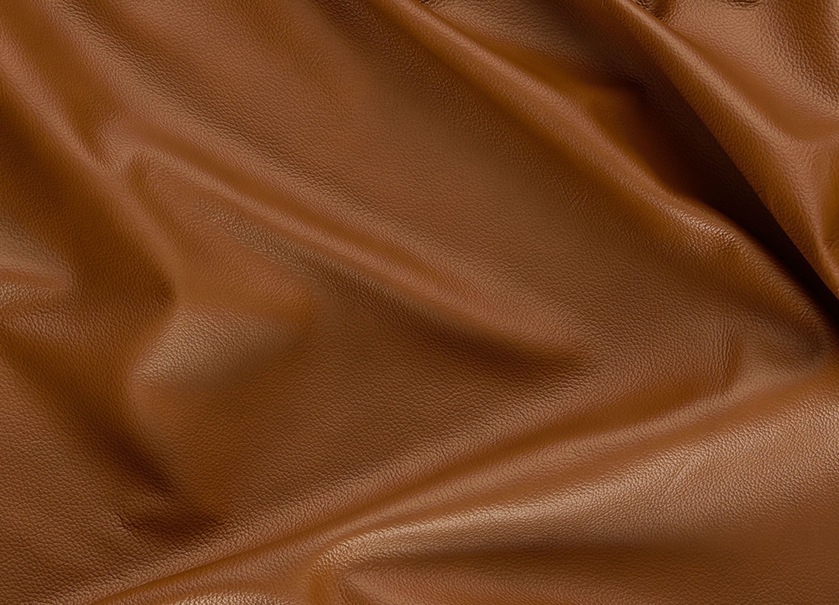 A close-up of draped brown faux leather fabric with a smooth, pebbled texture and soft folds.