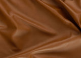 A close-up of draped brown faux leather fabric with a smooth, pebbled texture and soft folds.