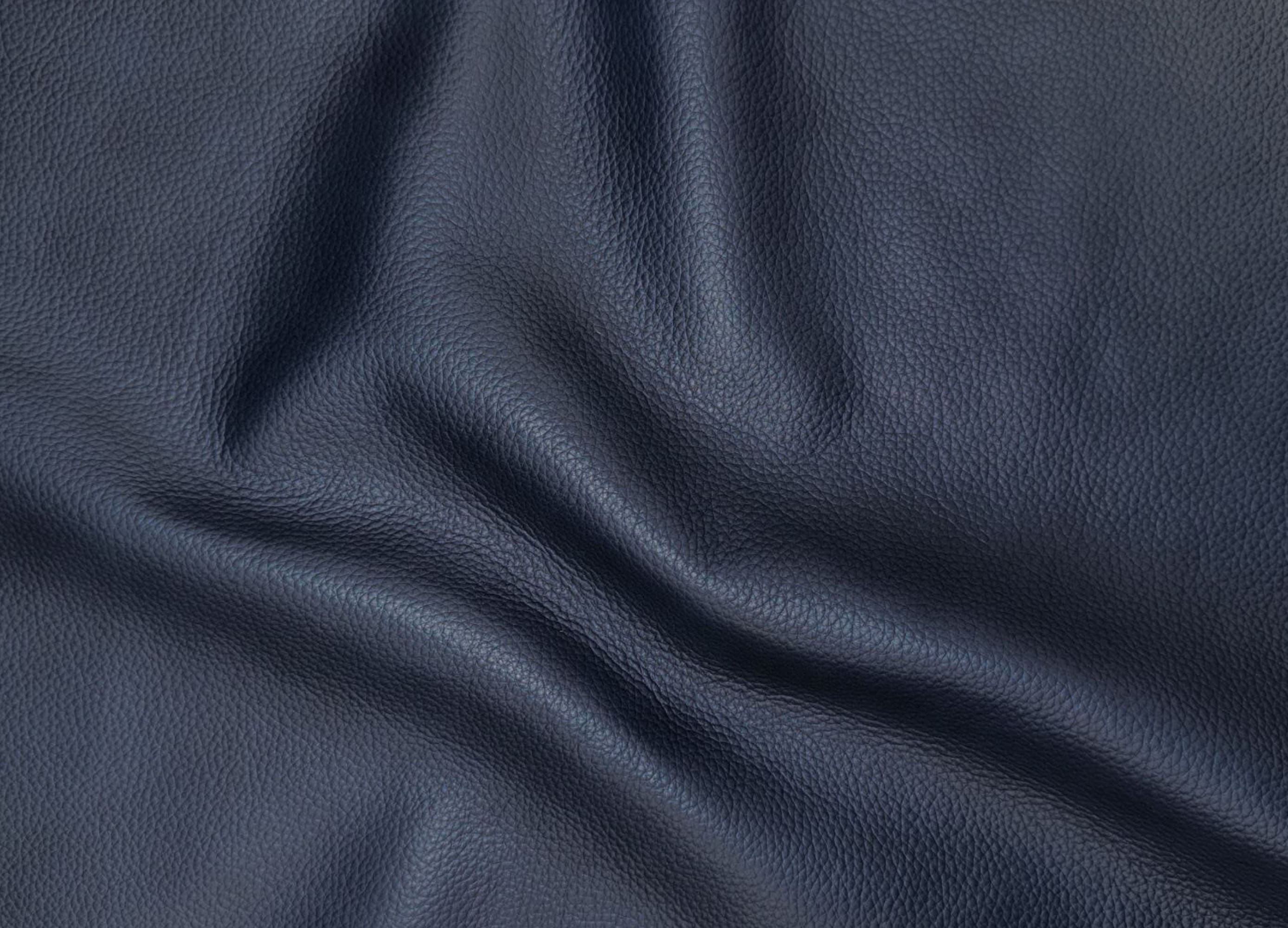 A close-up of dark navy blue textured leather fabric with soft folds and creases.