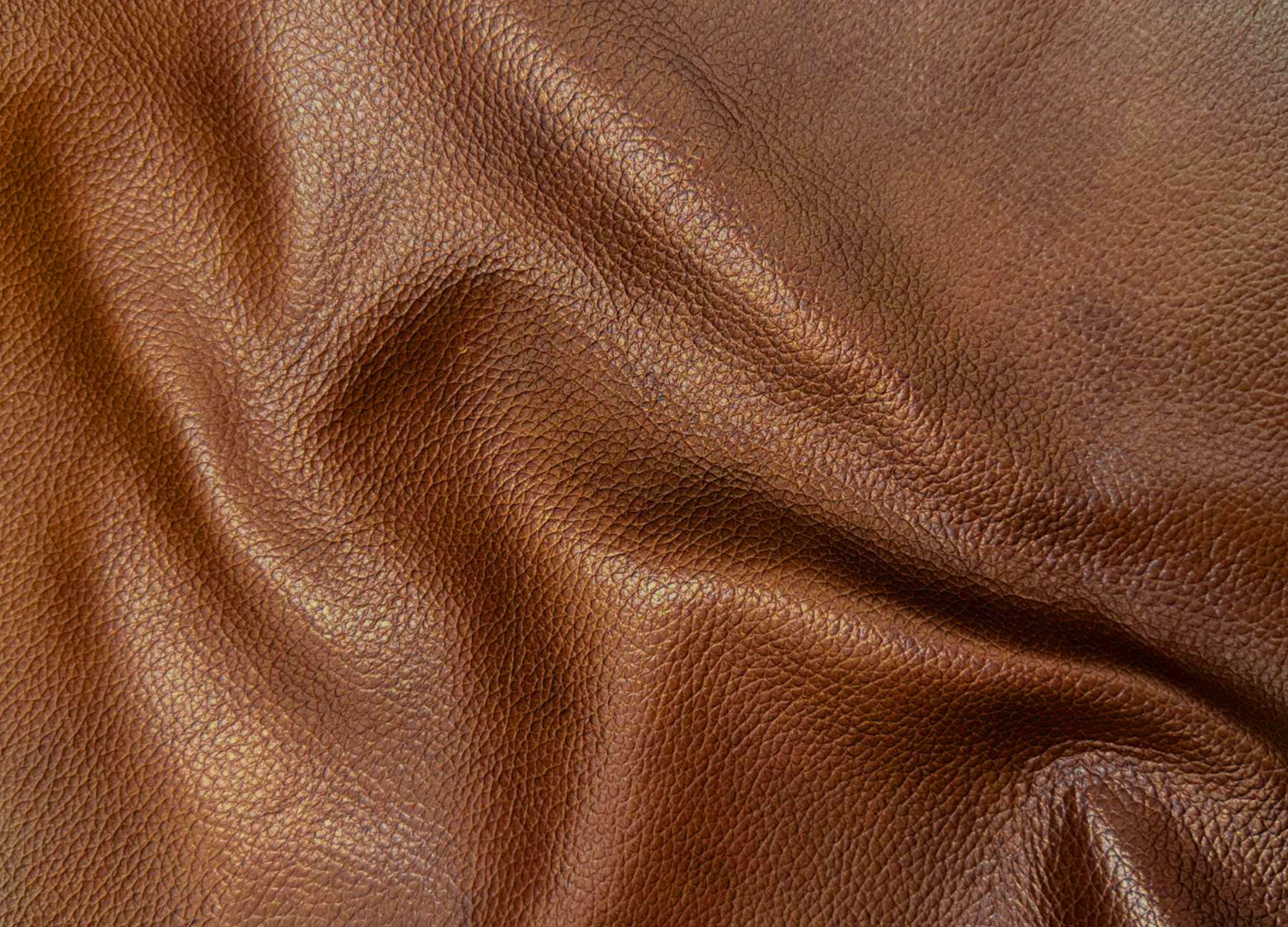 A close-up of draped brown leather fabric showing its pebbled texture and soft folds.