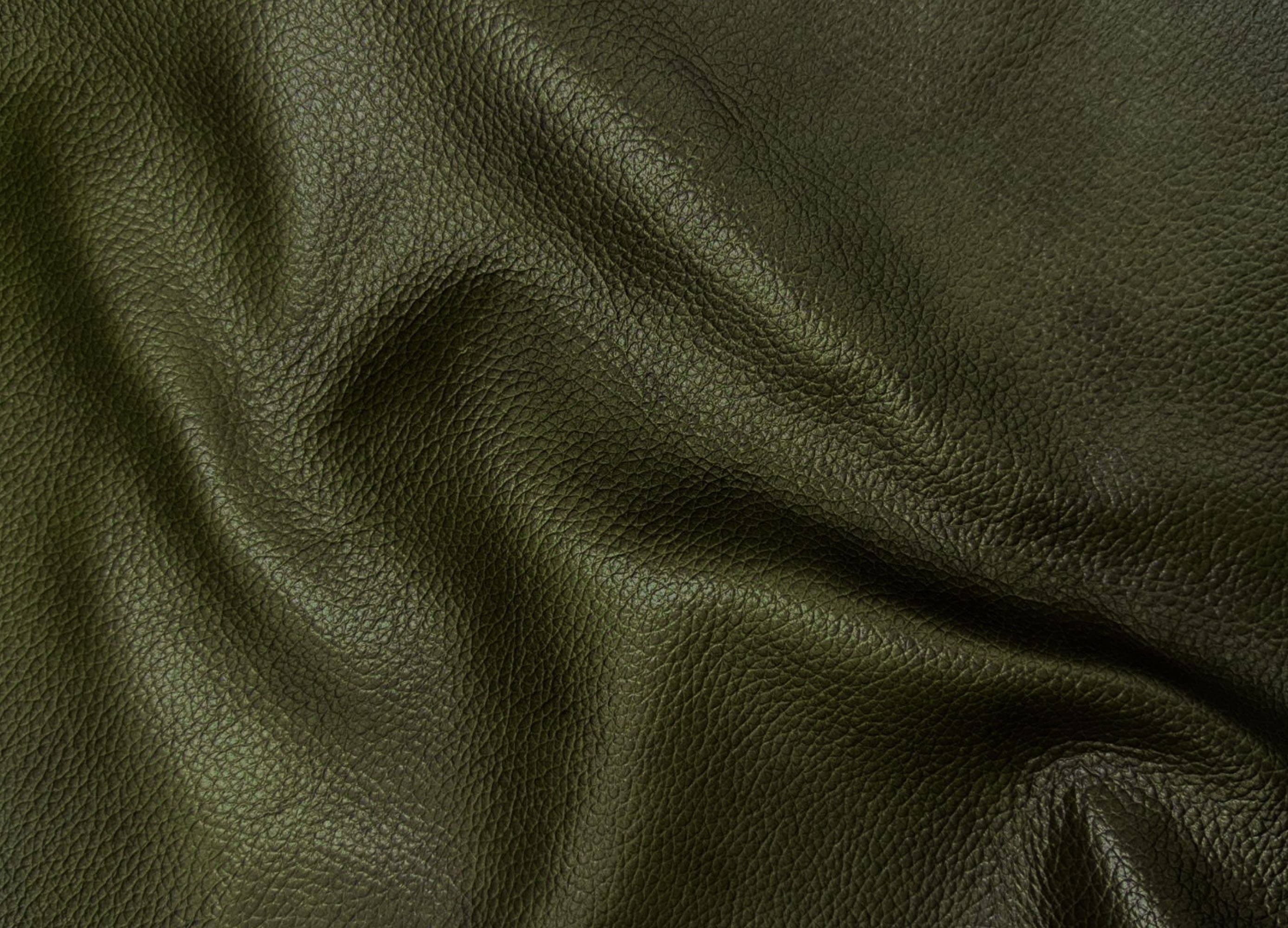 A close-up of dark olive green pebbled leather fabric with soft folds and shadows.