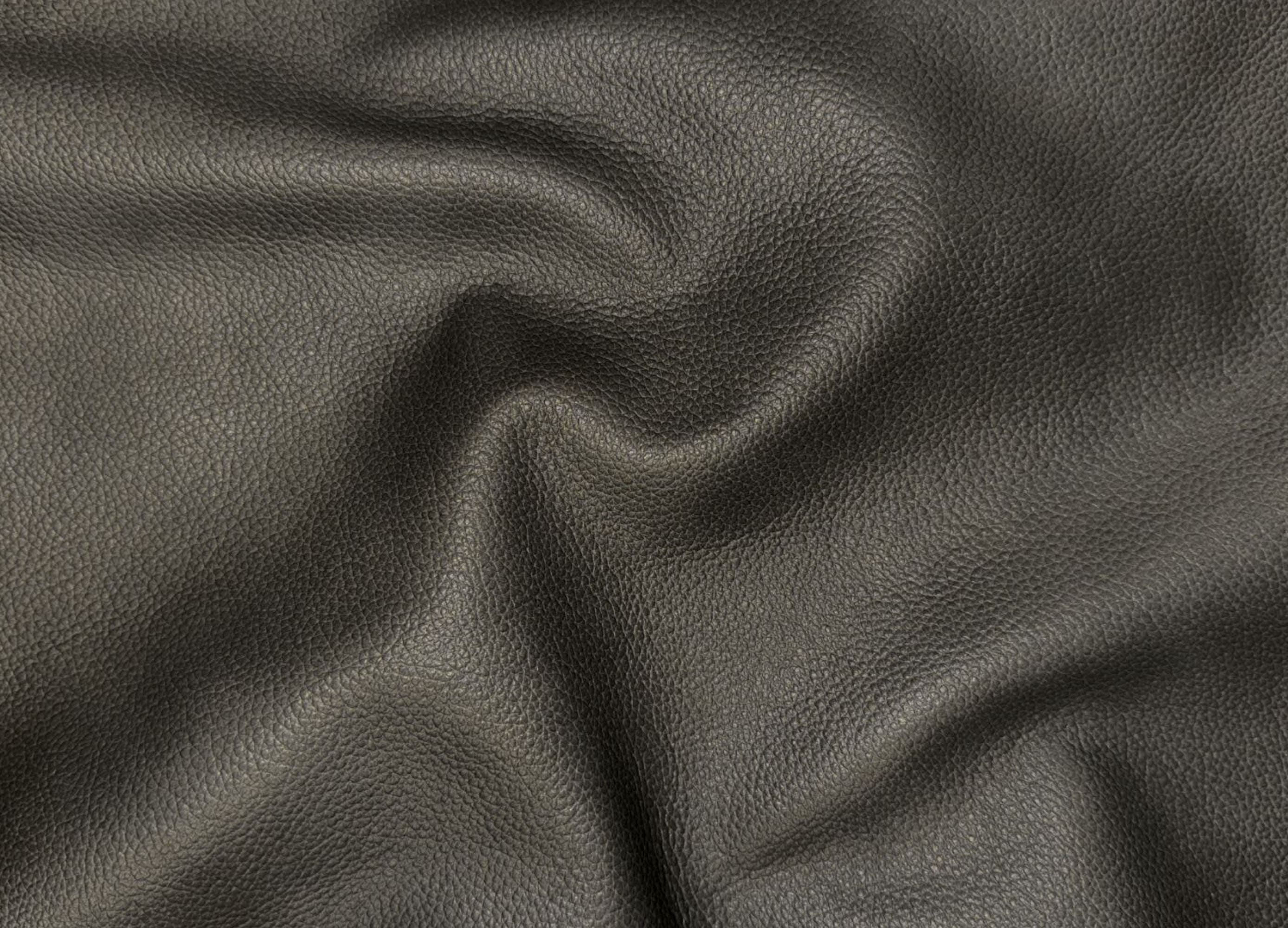 A close-up of dark charcoal gray textured leather fabric with soft folds and a pebbled grain surface.