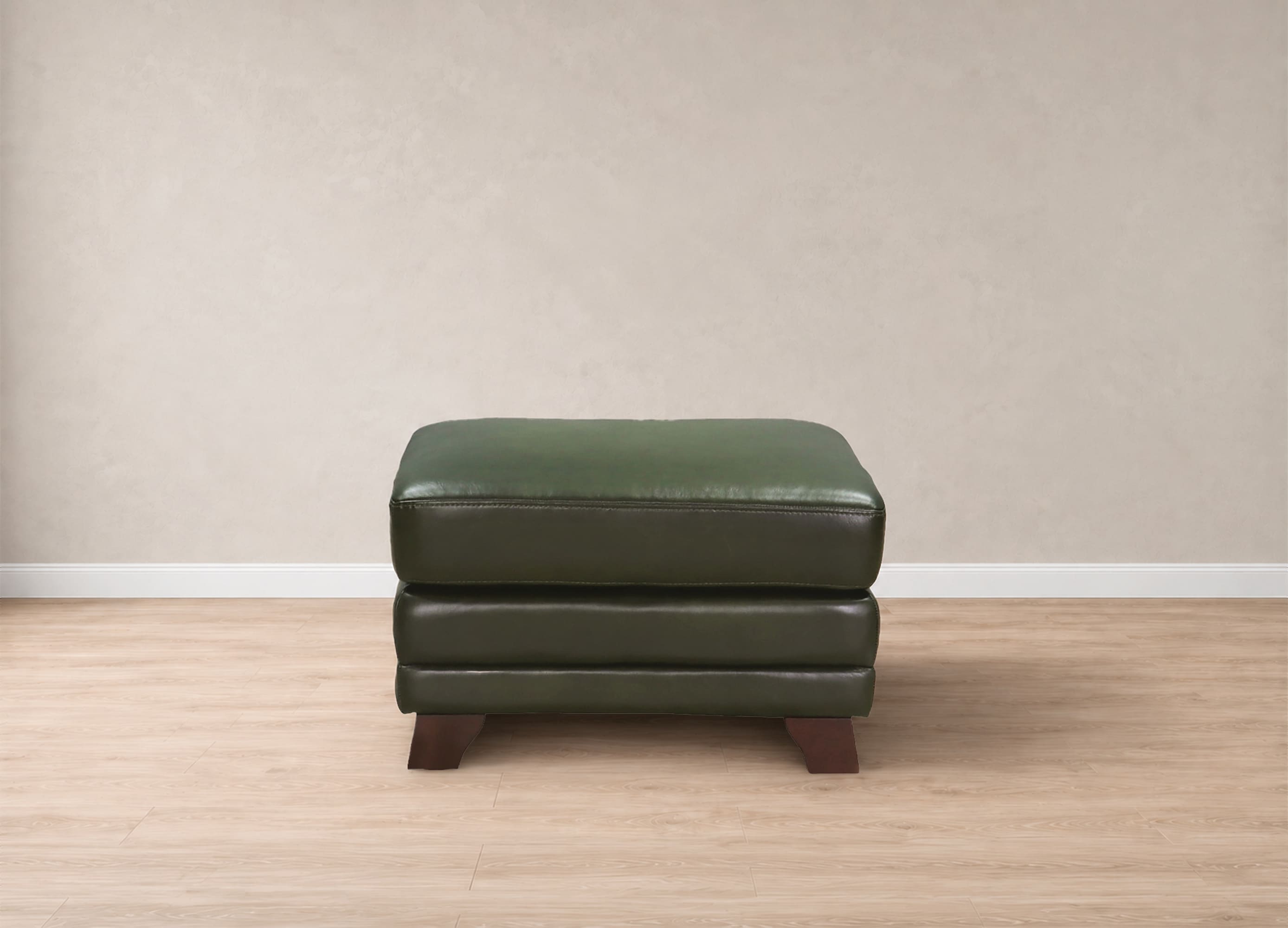 A dark green leather ottoman with stacked cushioned seats and dark wooden legs, positioned against a neutral beige wall and light wood floor.