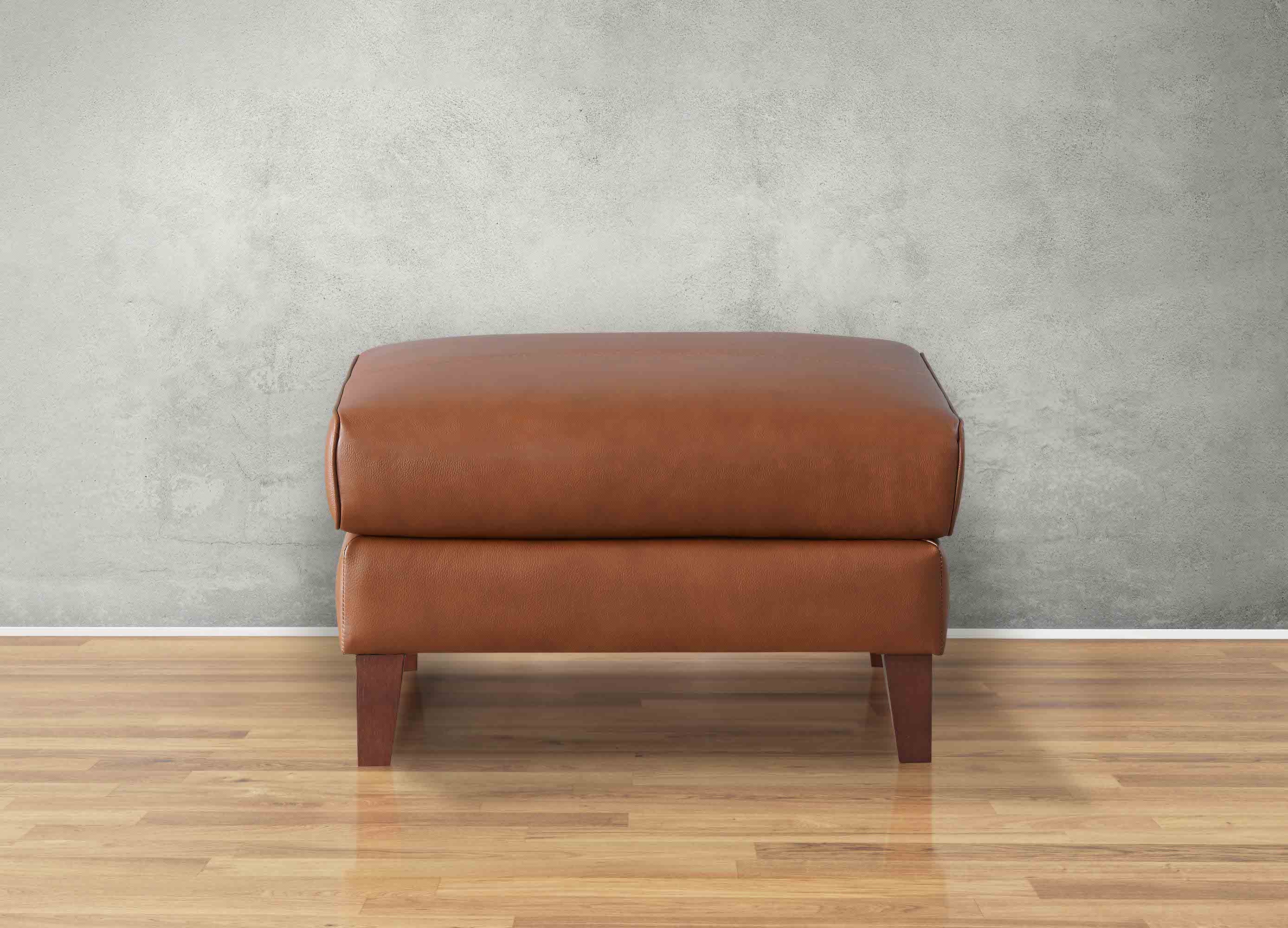 Brown leather ottoman on a wooden floor with a gray wall background