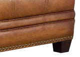 Close-up of a brown leather ottoman with nailhead trim on a white background