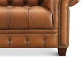 Brown leather sofa with tufted backrest and nailhead trim on a white background