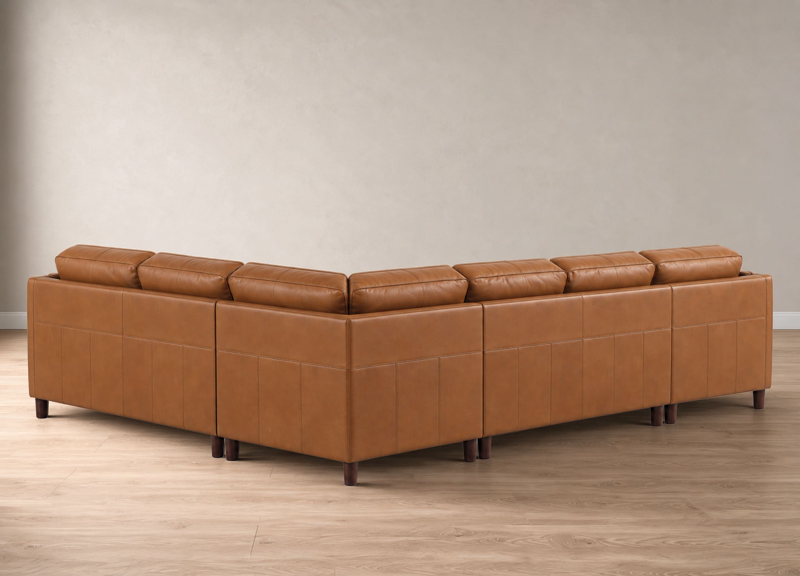 A modern L-shaped sectional sofa upholstered in warm tan leather, shown from a three-quarters angle against a neutral beige wall and light wood floor.