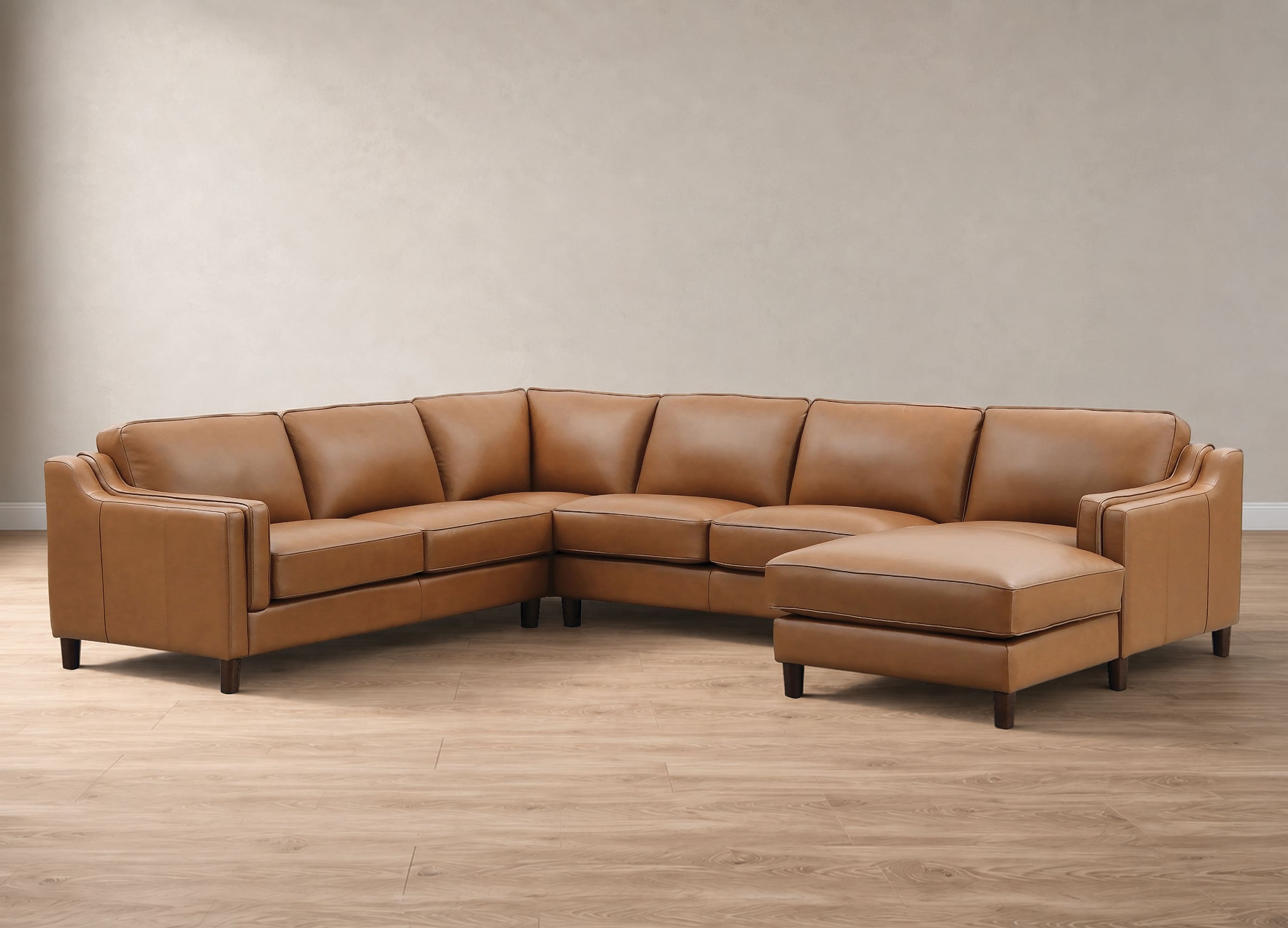 A modern L-shaped sectional sofa upholstered in warm tan leather, featuring a matching chaise ottoman, set against a neutral beige wall and light wood floor.