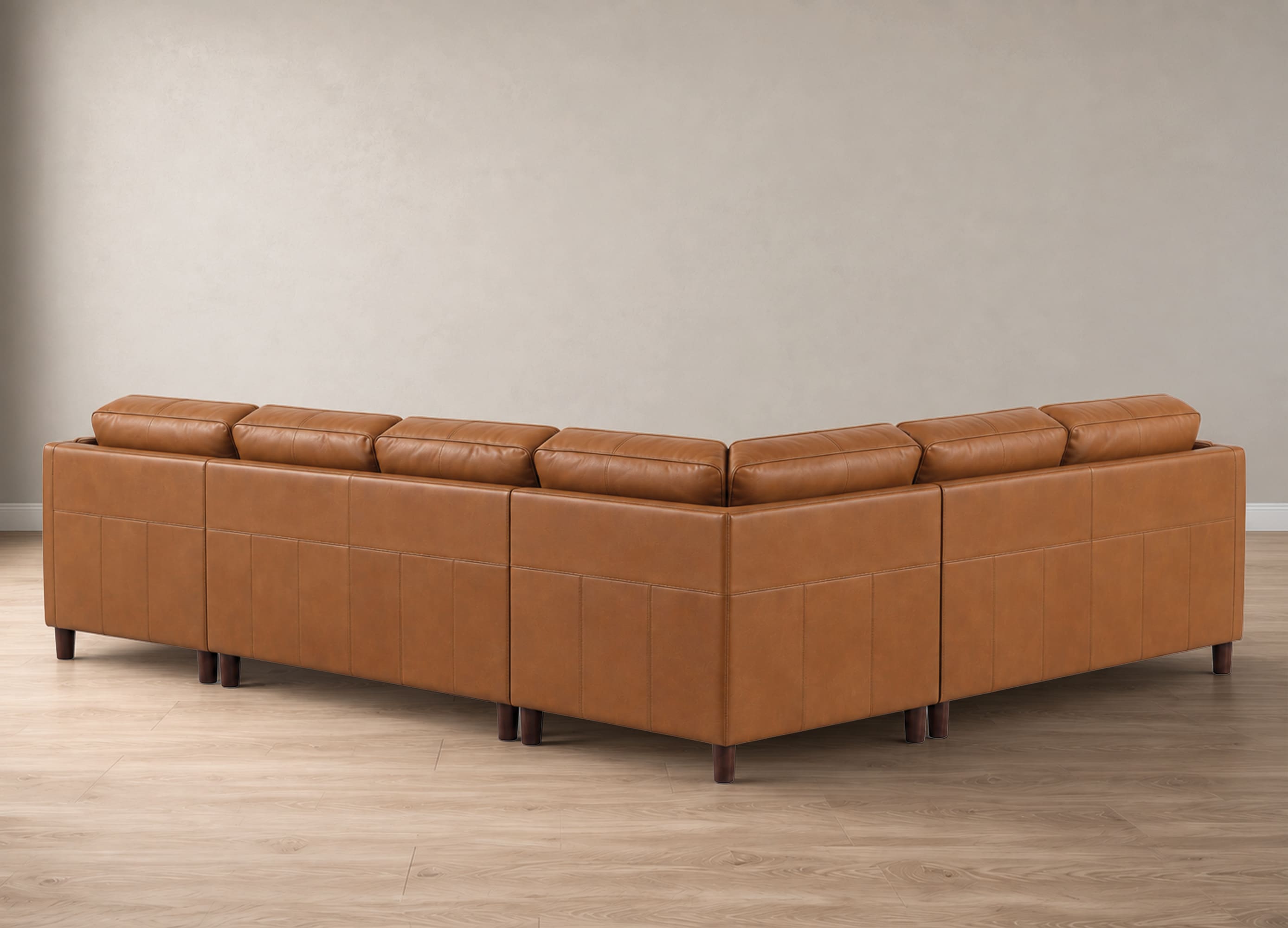 A modern L-shaped sectional sofa upholstered in warm tan leather, shown from a three-quarters angle against a neutral beige wall and light wood floor.