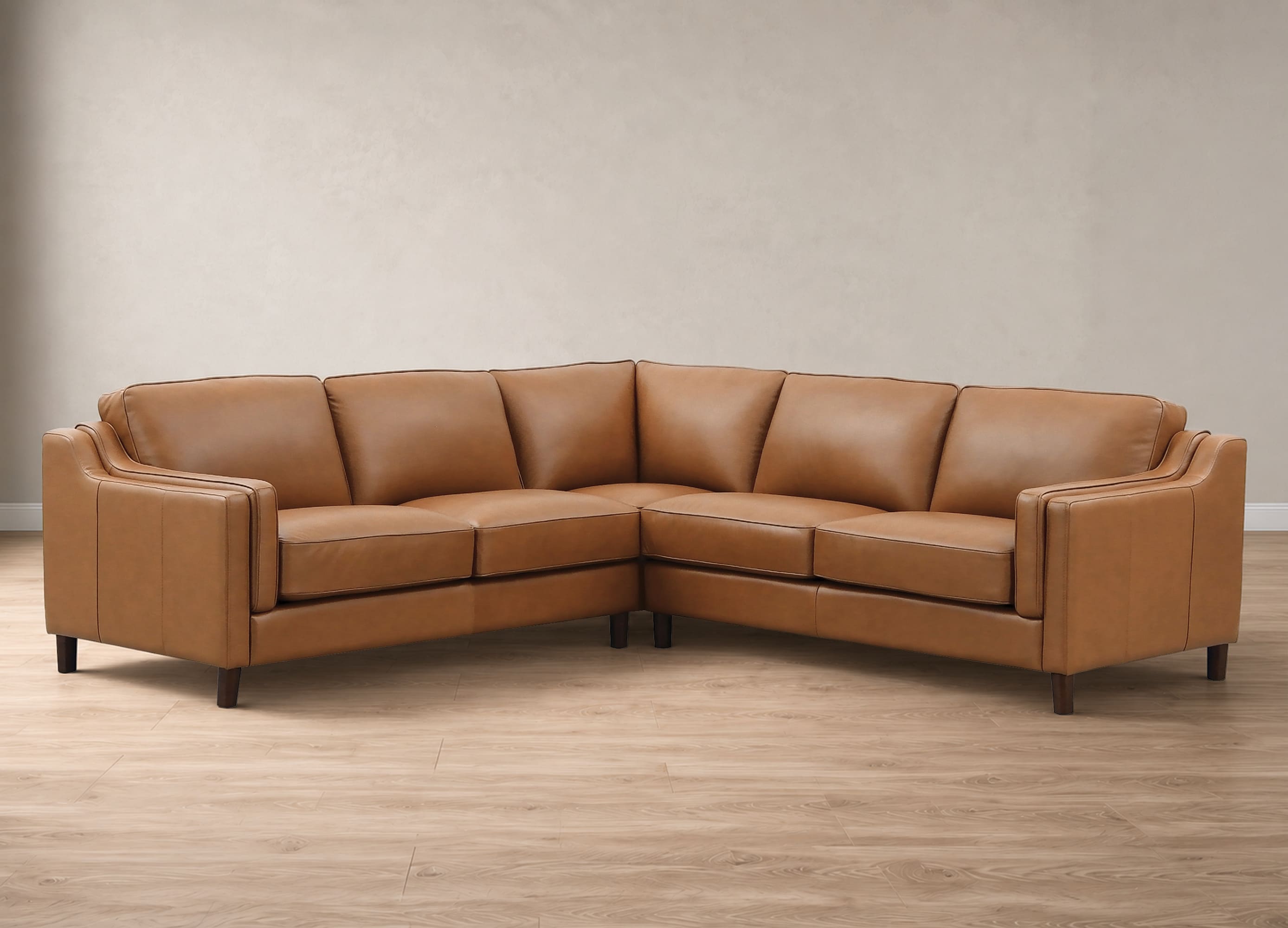 A tan leather sectional sofa with dark wooden legs, positioned in a room with a textured beige wall and light wood flooring.