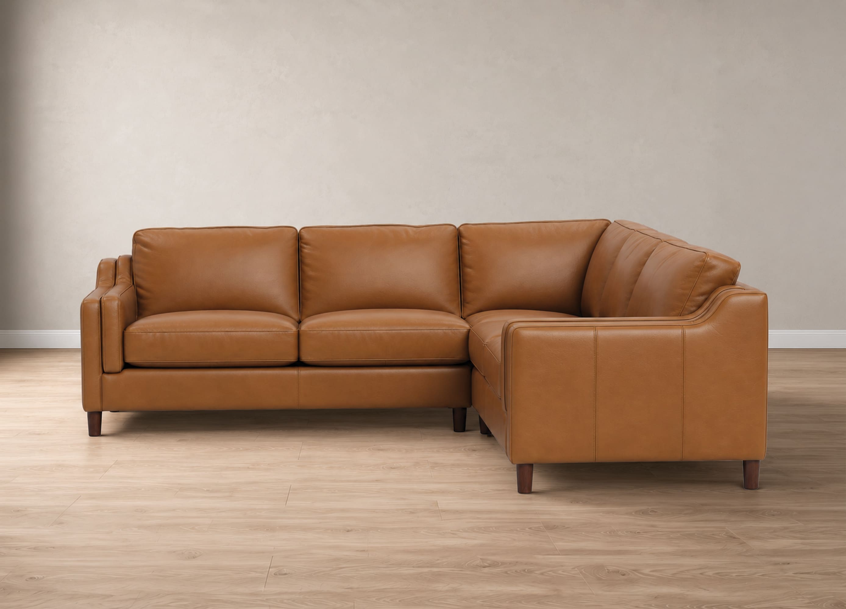 A modern three-seat sectional sofa upholstered in warm tan leather, positioned on a light wood floor against a neutral beige wall.