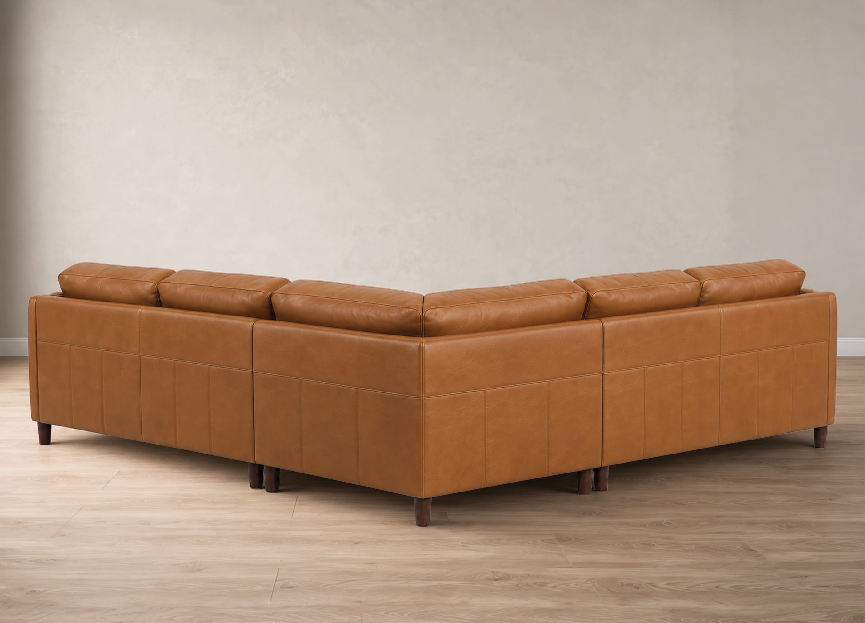 A modern sectional sofa upholstered in warm tan leather, shown from a three-quarters angle in a minimalist room with light wood flooring and a textured beige wall.